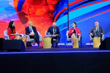 Pięć osób uczestniczy w panelu dyskusyjnym na scenie, jedna z nich przemawia do mikrofonu.